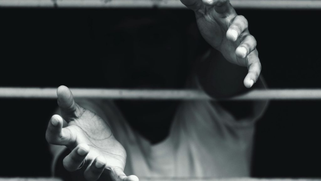 A person's hands reach through bars, symbolizing the struggle for freedom and community support in Los Angeles County.