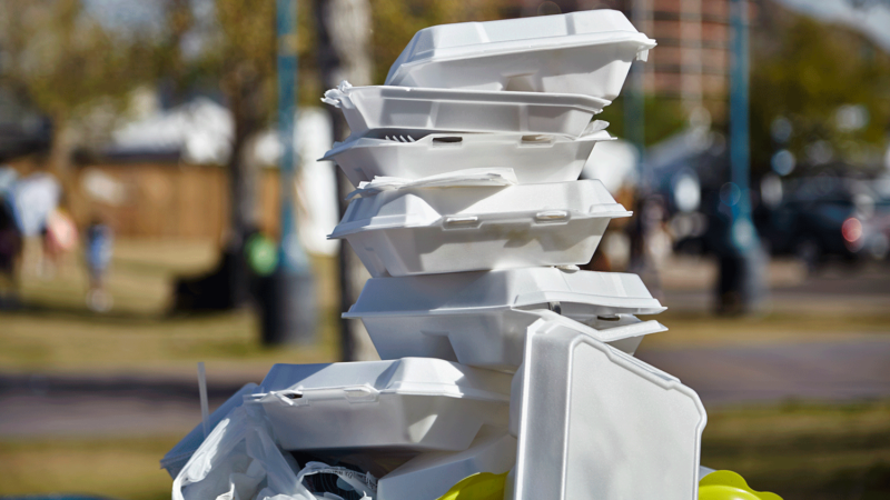 A stack of foam to-go boxes sit atop a trash can.