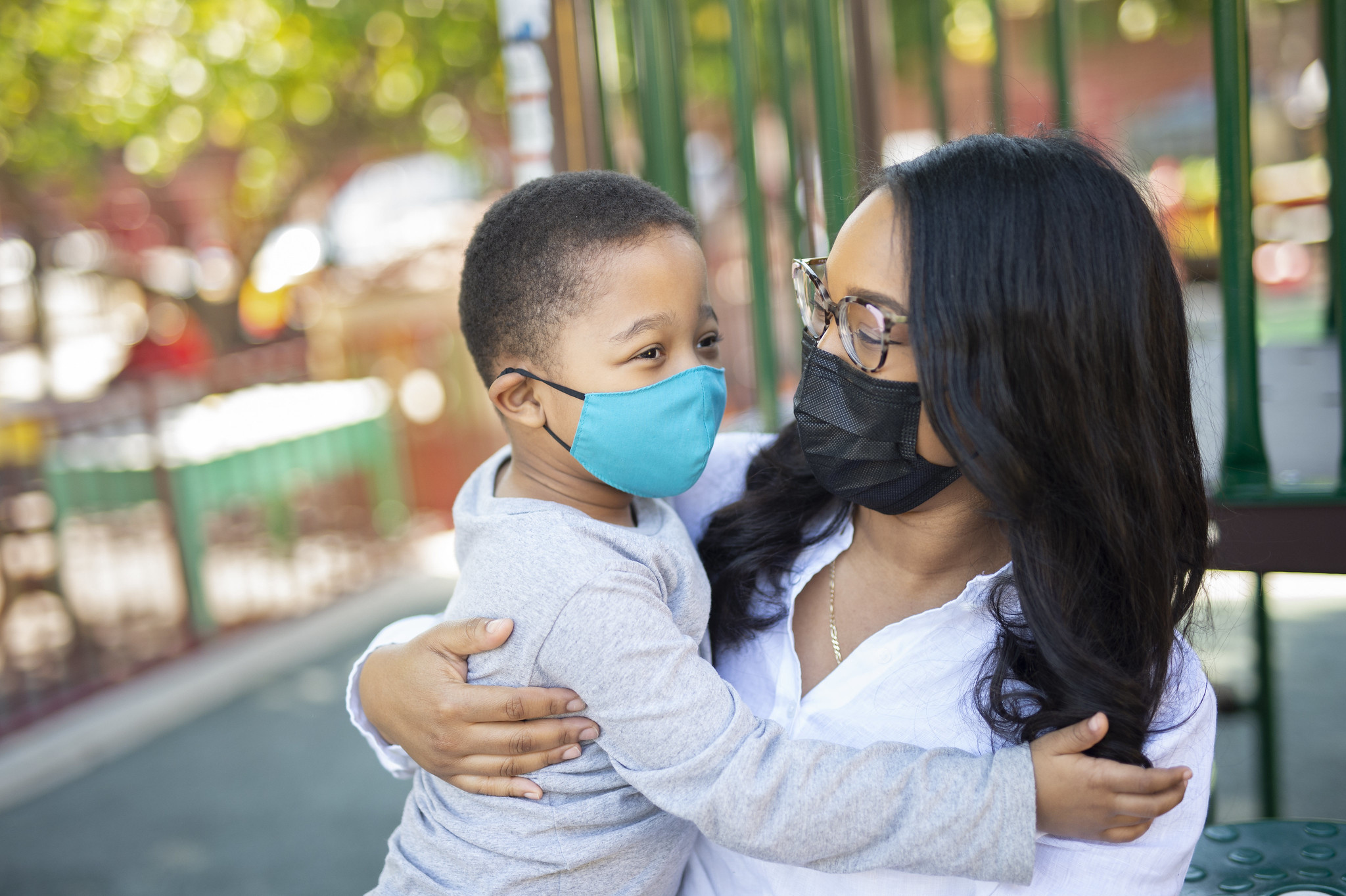 A caregiver and child share a moment at a playground, both wearing masks, highlighting community safety and connection.