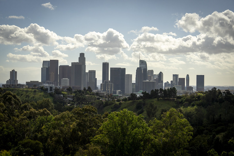 Downtown Los Angeles skyline viewed from a green hillside park under a partly cloudy sky