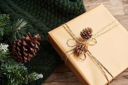 A beautifully wrapped gift adorned with pinecones, surrounded by greenery, symbolizing community celebration and togetherness.